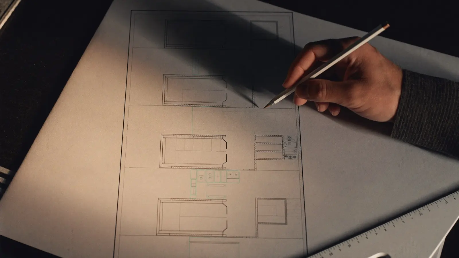 Mano de arquitecto dibujando a lápiz la planta de un hospital, con salas de operaciones alineadas a lo largo de un pasillo central